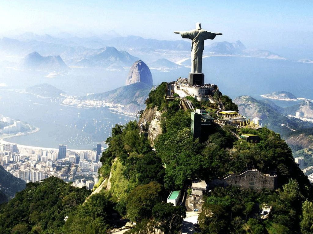Foto aérea do Cristo Redentor de costas com uma bela visão da orla do Rio de Janeiro e o Pão de Açúcar no fundo