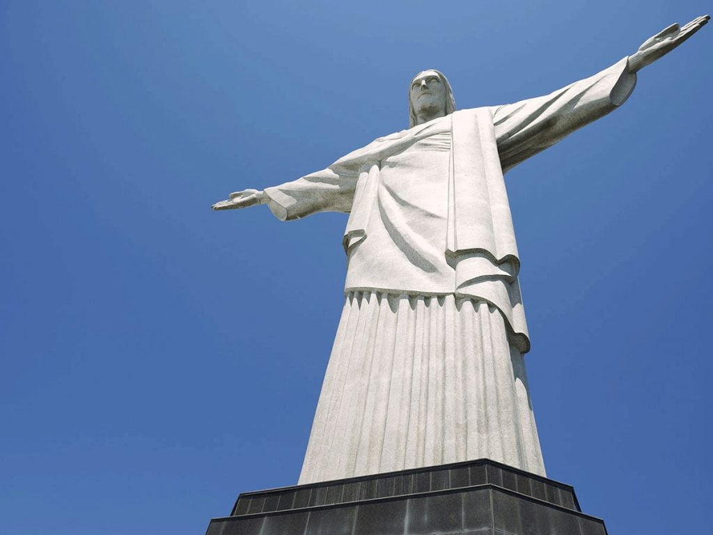 Foto do Cristo Redentor tirada de frente e de baixo, mostrando o céu azul sem nuvens